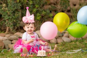 beautiful baby girl in pink birthday hat holding balloons